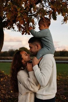 a man and woman holding a baby under a tree