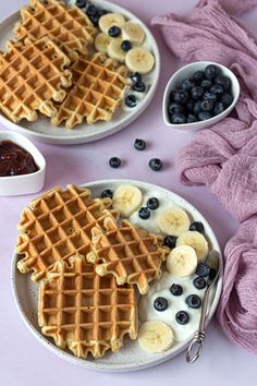 two waffles with bananas and blueberries on a plate next to some fruit