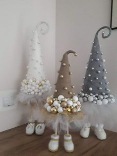 three small christmas trees with white and gold decorations on them, one is wearing shoes