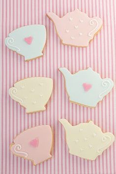 four decorated cookies sitting on top of a pink and white striped tablecloth with teapots