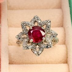 a ring with a large red stone surrounded by small white diamonds in a velvet box