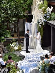 a couple is getting married in front of an outdoor ceremony area with white flowers and greenery