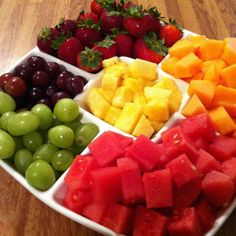 a platter filled with different types of fruit on top of a wooden table next to strawberries and grapes