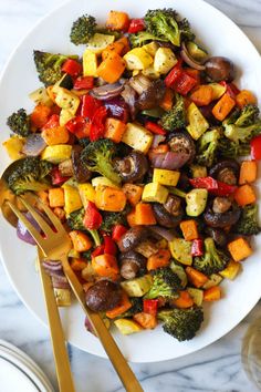 a white plate topped with veggies next to two golden utensils on top of a marble counter