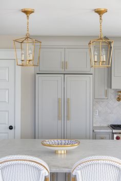 a kitchen with white cabinets and gold accents on the counter top, along with two pendant lights hanging from the ceiling