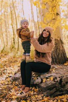 a woman sitting on top of a rock in the woods holding a child up to her chest