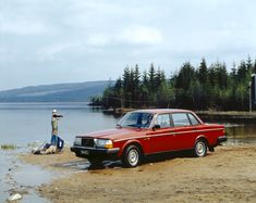 a man standing next to a red car on top of a sandy beach