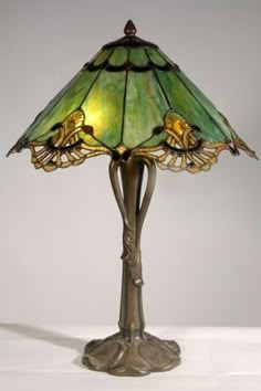 a lamp that is sitting on top of a white tablecloth and has a green glass shade over it