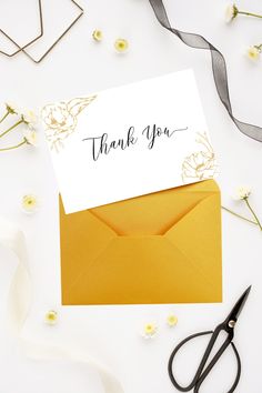 a thank you card sitting on top of an envelope next to some scissors and flowers