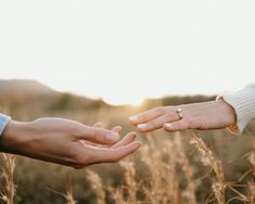 two people reaching out their hands to each other in the middle of an open field