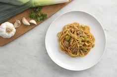 a white plate topped with pasta next to an onion and celery leaf on top of a wooden cutting board