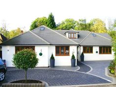 a white house with two cars parked in front of it and trees around the driveway