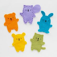 four different colored felt animals on a white surface with one bear and the other rabbit