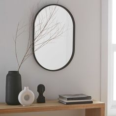 a mirror on the wall above a table with a vase and book next to it