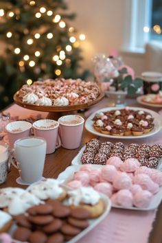 a table topped with lots of desserts and drinks next to a christmas tree in the background