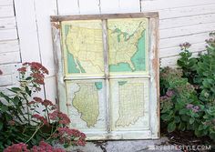 an old window with a map on it in front of some plants and flowers outside