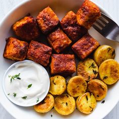 a white plate topped with potatoes and tofu next to a bowl of ranch dressing