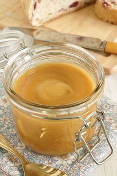 a glass jar filled with peanut butter sitting on top of a table next to sliced bread