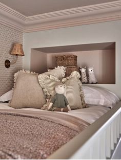 a bed with pillows and stuffed animals on top of it in a room that has white walls