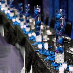 the table is set up with blue flowers and candles in tall vases on each side