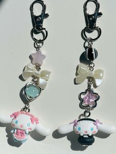 two key chains with charms attached to them on a white surface and one has a pink bow