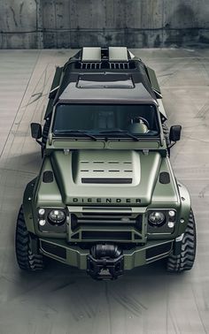 an army green truck parked on top of a parking lot next to a cement wall