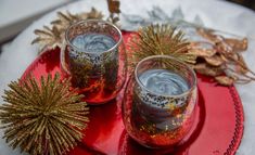 two wine glasses sitting on top of a red plate next to dry leaves and an acorn