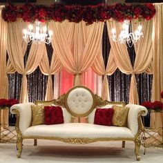 a white couch sitting under a chandelier in front of a red rose covered window