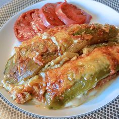 a white plate topped with meat covered in sauce next to tomatoes and green beans on top of a table