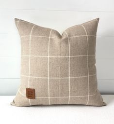 a brown and white plaid pillow with a leather patch on the front, sitting on a bed