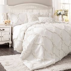 a white bed in a bedroom next to a night stand with flowers on the nightstand