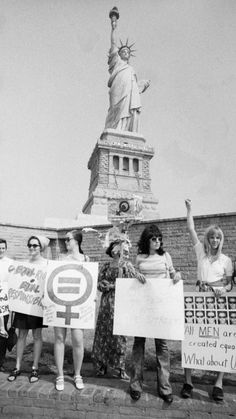 black and white photograph of people holding signs in front of the statue of liberty