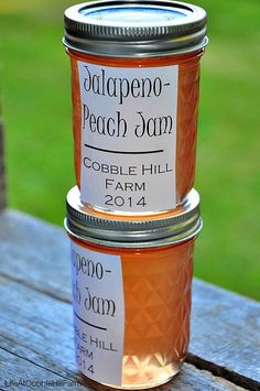 two jars of peach jam sitting on top of a wooden table in front of grass