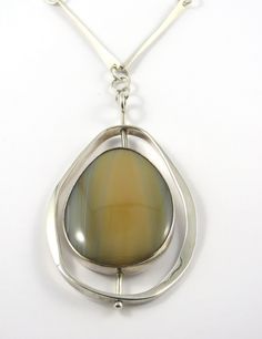 This is a modern designed sterling silver bezel set swivel Agate pendant with a 24 inch chain. The large tear shaped cabochon cut agate has various hues of light brown and gray colors in it and is bezel set. The outer egg shaped silver border is attached to the center with a silver bar that  allows the pendant to swivel. The back of the pendant is closed and is signed " rme sterling 1975". The 24 inch chain is made up of long twisted silver bars and each link is connected by  large round jump ri Contemporary Oval Jewelry With Polished Finish, Contemporary Teardrop Silver Jewelry, Modern Teardrop Large Pendant Necklaces, Modern Brown Gemstone Jewelry, Modern Jewelry With Round Cabochon Pendant, Modern Cabochon Round Pendant Jewelry, Modern Chalcedony Jewelry With Polished Finish, Modern Cabochon Round Pendant, Modern Oval Large Pendant Jewelry