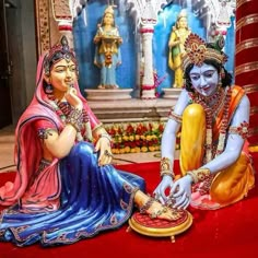 two statues of hindu deities sitting on a red carpet