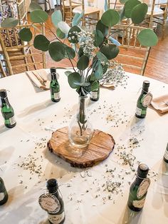 a table topped with lots of bottles filled with flowers and greenery sitting on top of a white table cloth