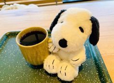 a stuffed dog sitting on top of a green tray next to a cup of coffee