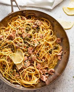 a pan filled with pasta and meat on top of a table next to sliced lemons