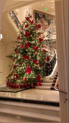 a decorated christmas tree sitting in the middle of a room next to a stair case