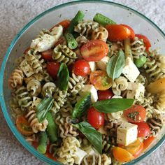 a glass bowl filled with pasta salad on top of a white carpeted tablecloth