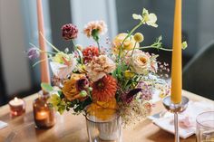 a vase filled with flowers sitting on top of a wooden table next to two candles