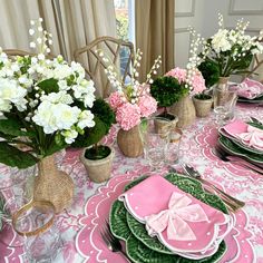 a table set with pink and green plates, napkins and flowers in vases