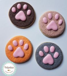 four decorated cookies with pink and purple icing on top of each cookie, one has an animal's paw