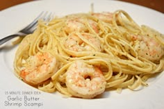 a white plate topped with pasta and shrimp next to a fork on top of a wooden table