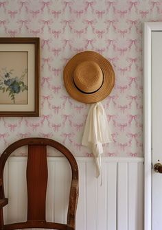 a hat is hanging on the wall next to a wooden chair and framed painting in a room