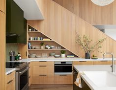 a kitchen with wooden cabinets and white counter tops under a stair case that leads up to the second floor