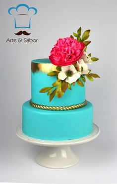 there is a blue cake with flowers on the top and gold trim around the edges