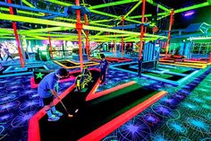 an indoor golf course is lit up with neon lights and people playing in the background