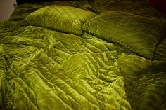 an unmade bed with green sheets and pillows