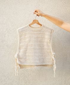 a woman holding up a white crochet top with tassels on it